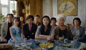An Asian family sits around a table full of fairly elaborate snacks. No one appears particularly happy.