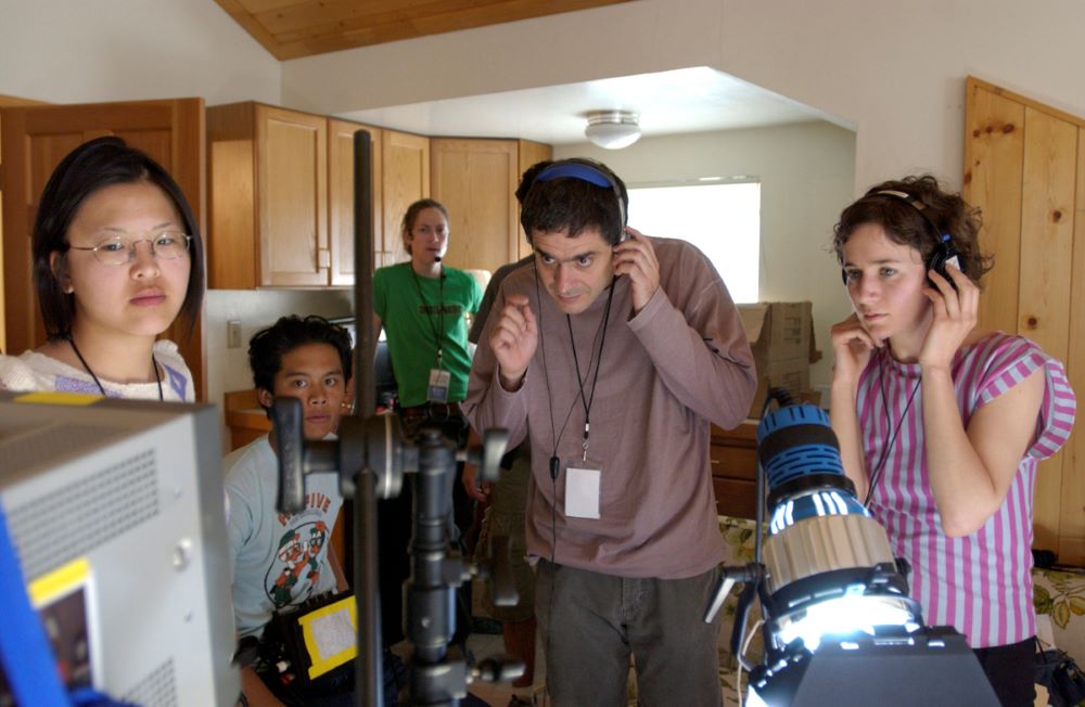 Five people, two with headsets, are watching a monitor, surrounded by equipment.