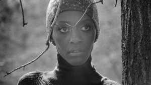 A black and white close up of a young Black woman, model Bethann Hardison, as she looks on.