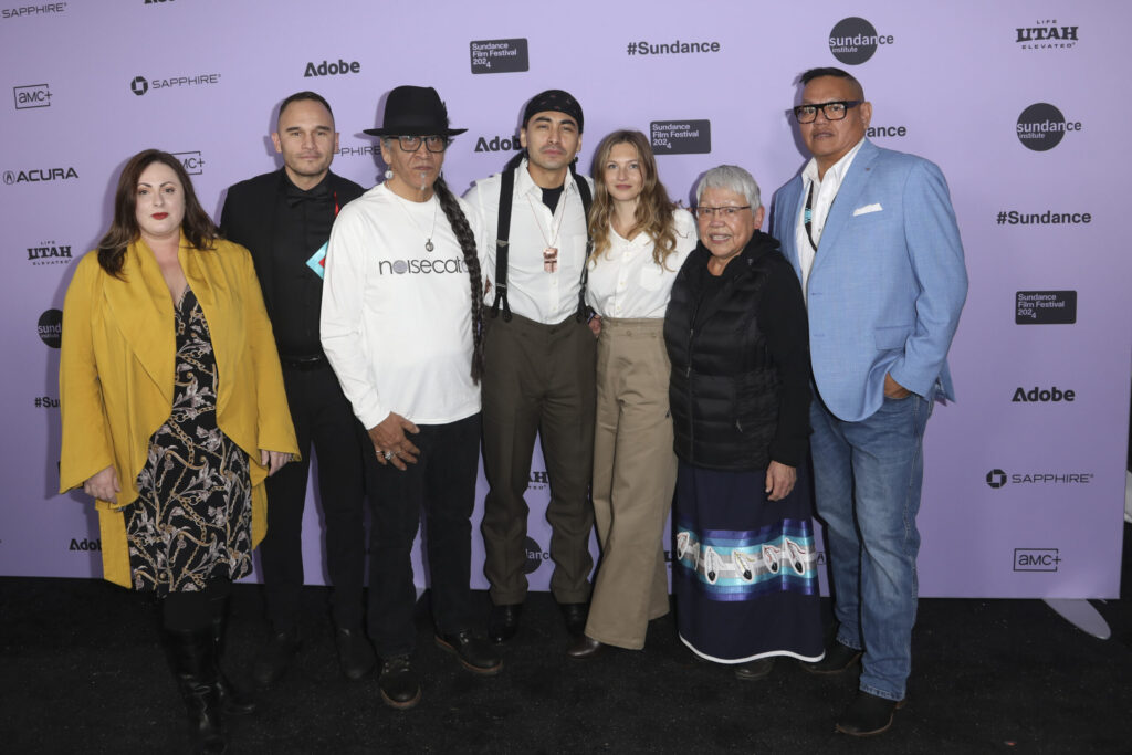 A group of seven people poses in front of a 2024 Sundance Film Festival backdrop