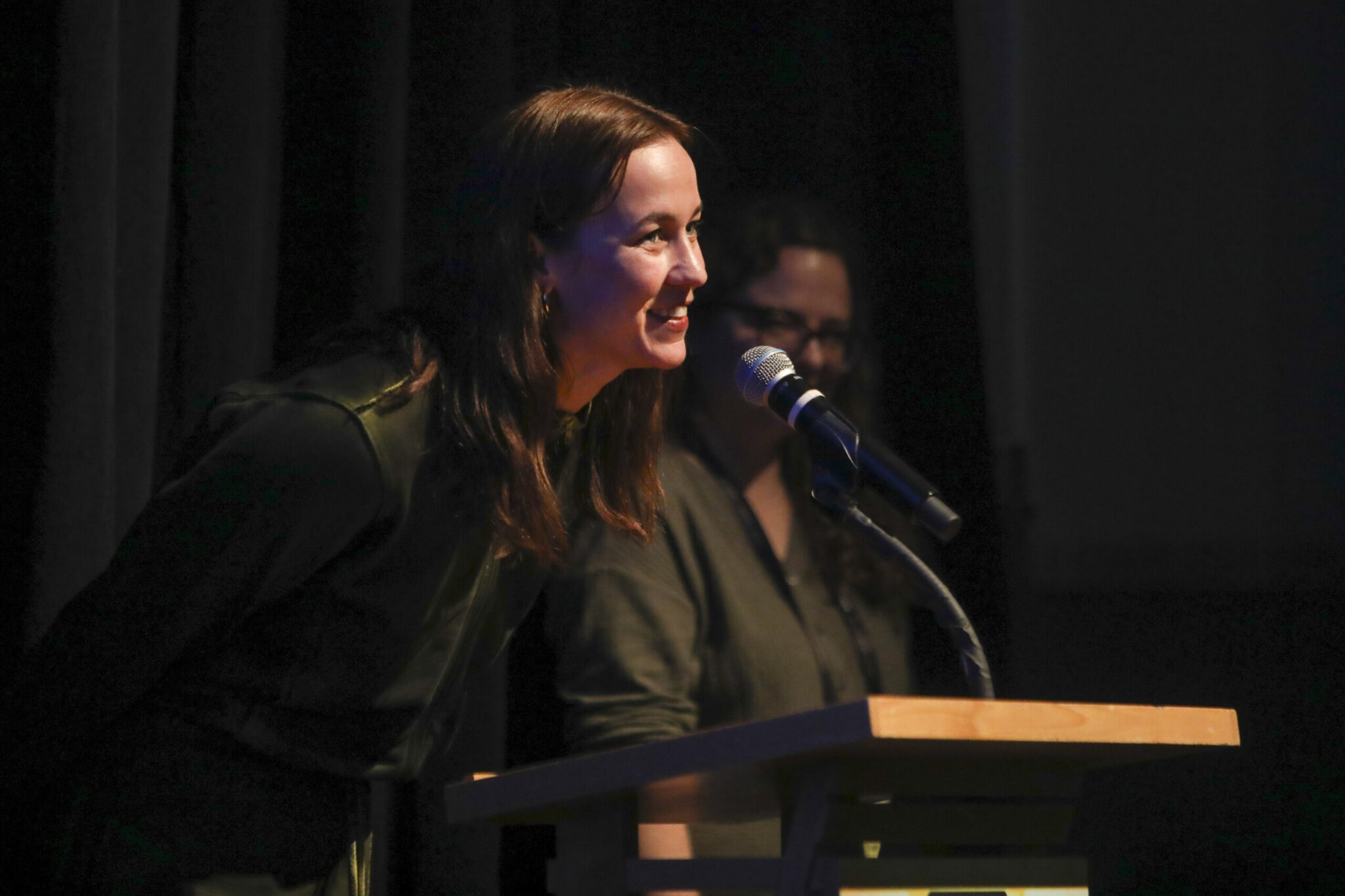 Woman with long brown hair steps to the microphone