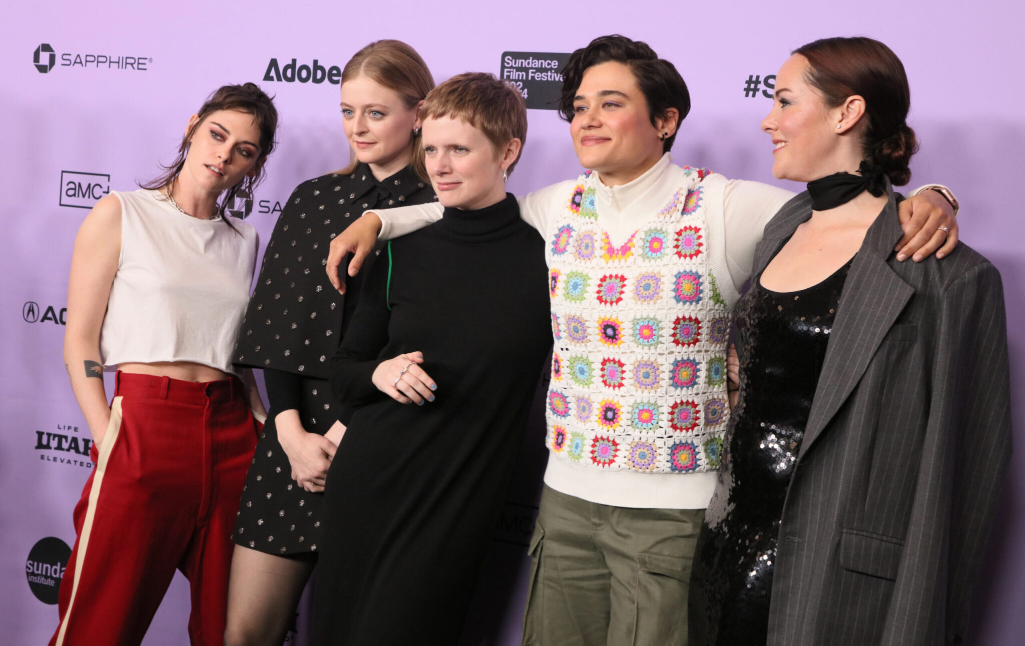 Kristen Stewart, Anna Baryshnikov, Rose Glass, Katy O’Brian, and Jena Malone pose in front of a white 2024 Sundance Film Festival backdrop.