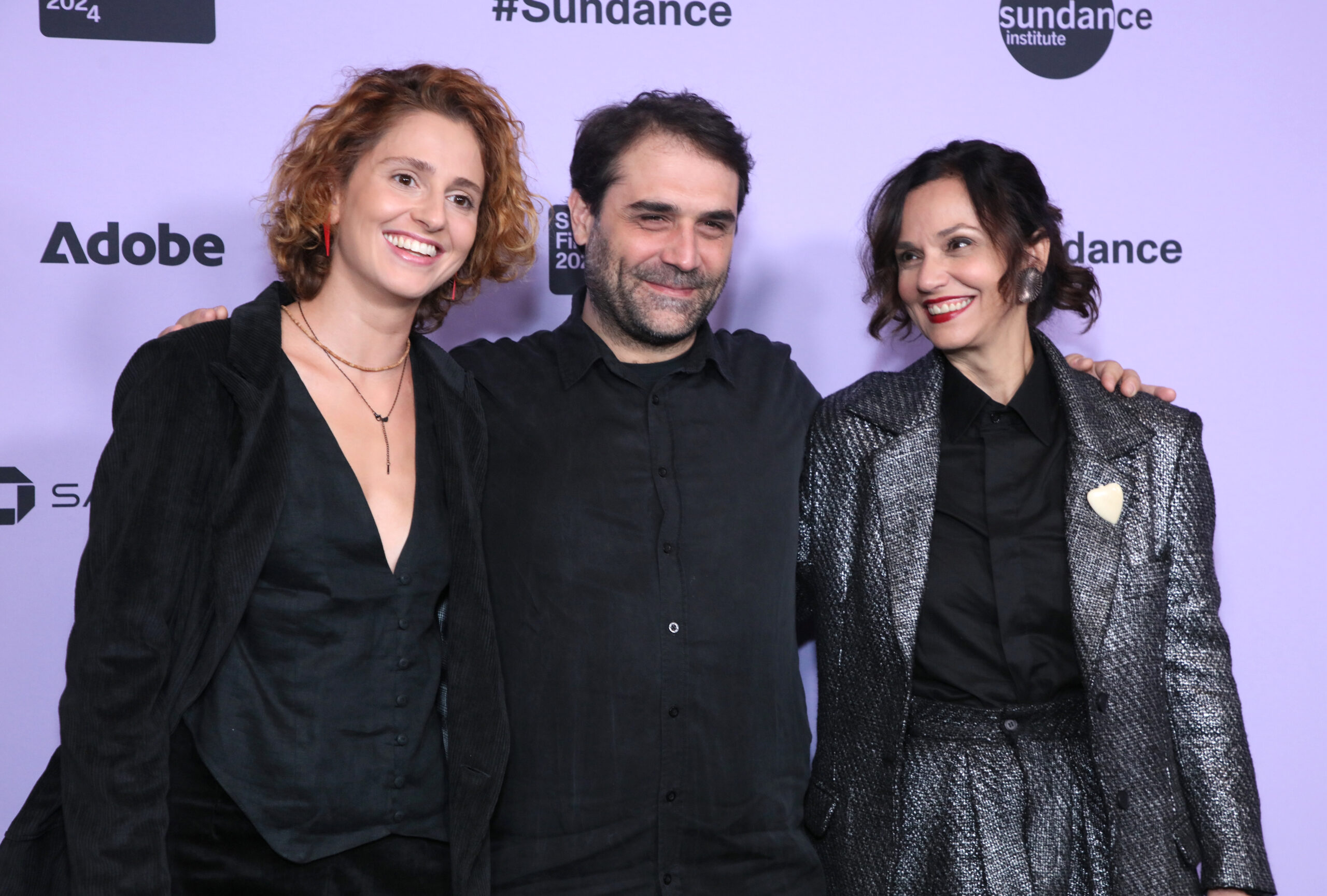 Two women flank a bearded man in front of a Sundance Film Festival backdrop.