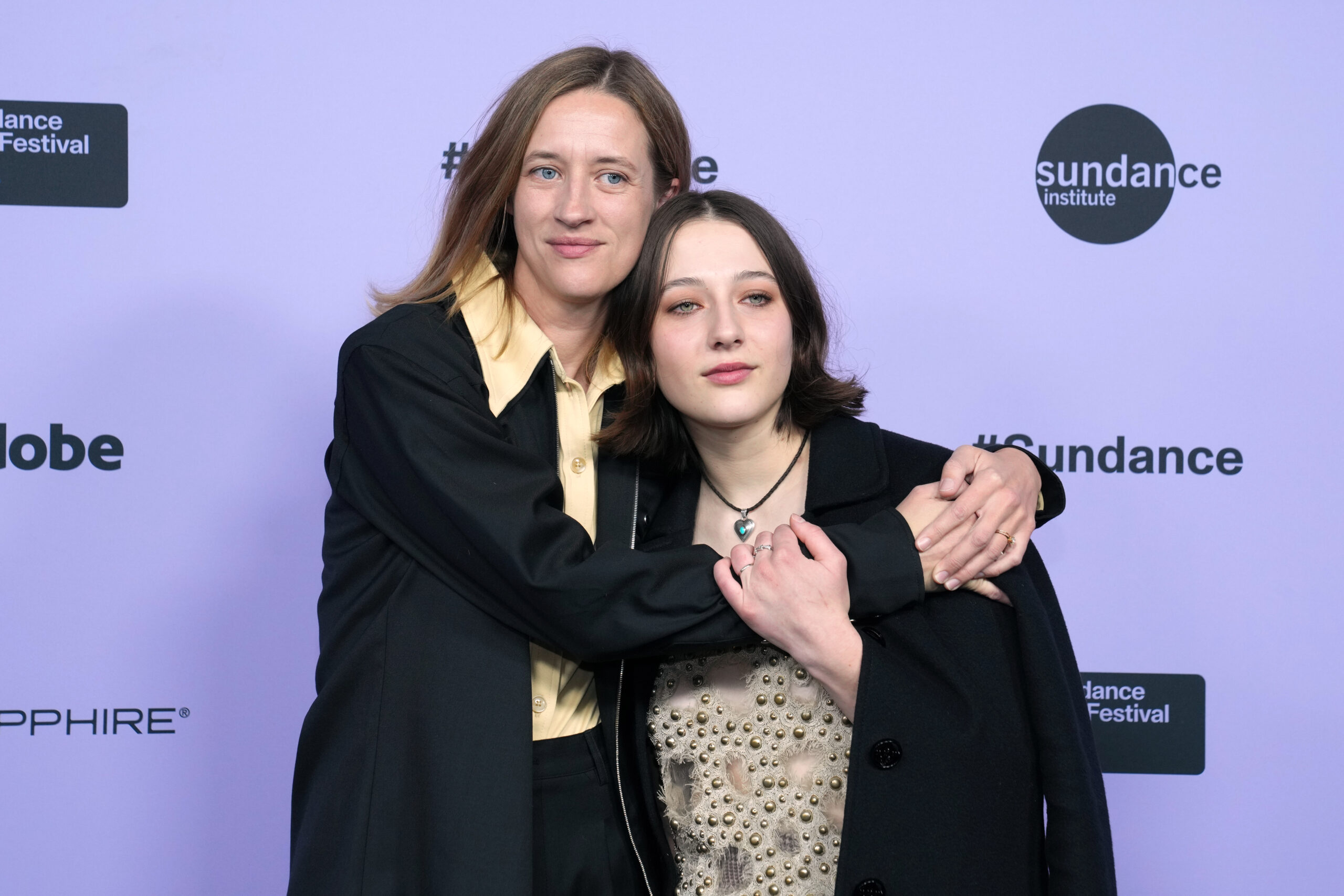 India Donaldson and Lily Collias hug in front of a white 2024 Sundace Film Festival backdrop.
