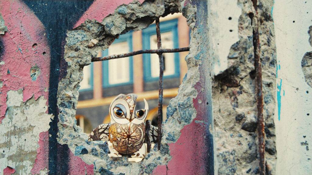 A small painted bird sculpture sits inside a hole in a concrete wall