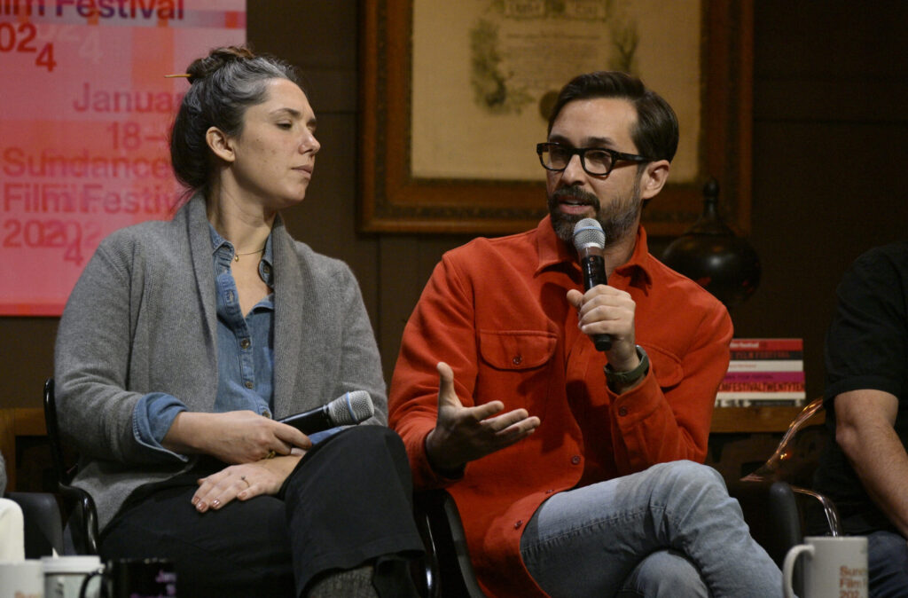 Sam Zuchero and Andy Zuchero are sitting in chairs at the Filmmaker Lodge. Andy Zuchero is speaking into a microphone.