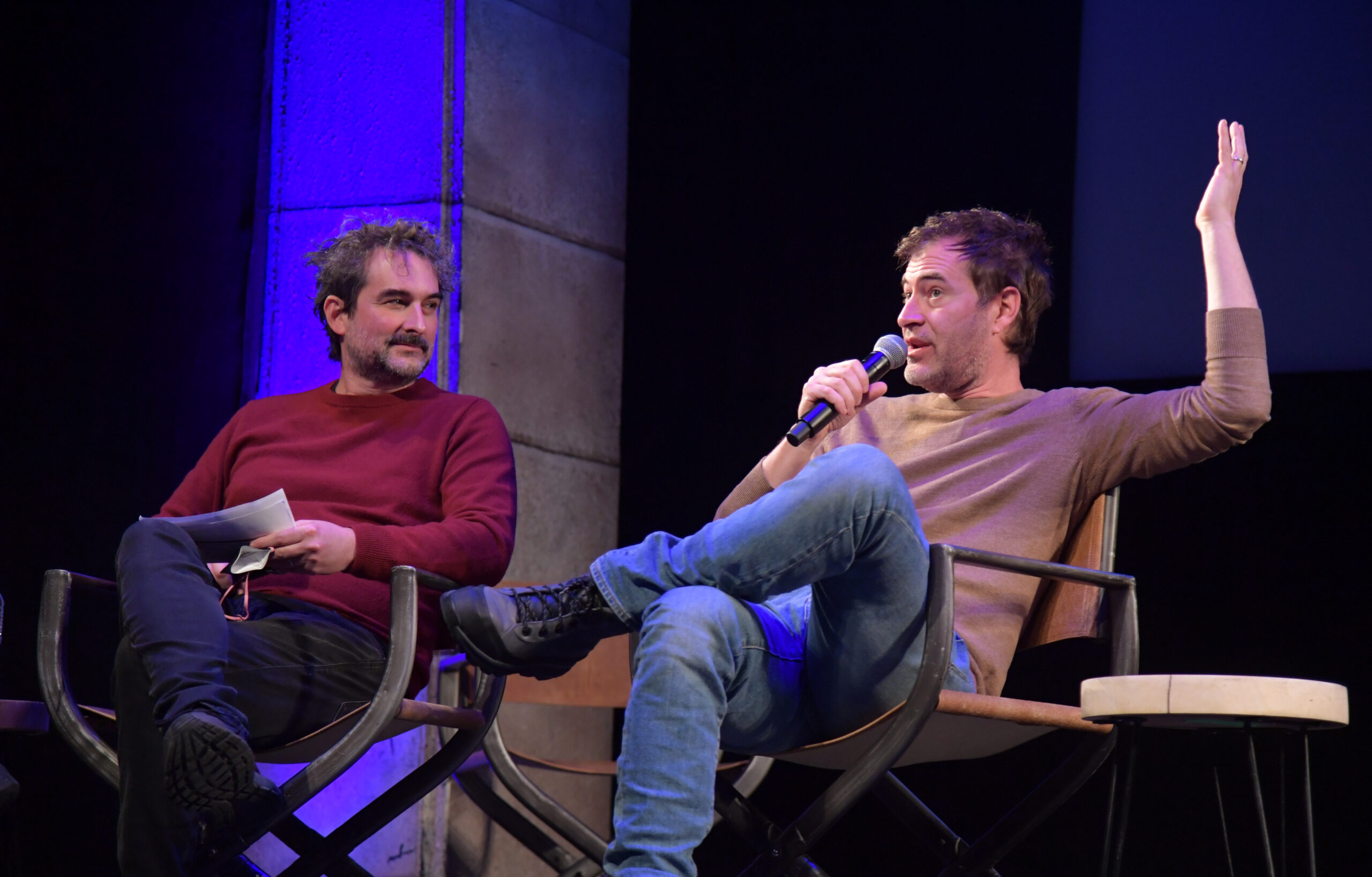 Jay Duplass and Mark Duplass sit on stage at the Egyptian Theatre. Mark Duplass is speaking into a microphone and waving his hand.