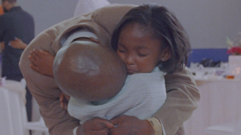 A close up of A Black man holding high young daughter who is in a white dress