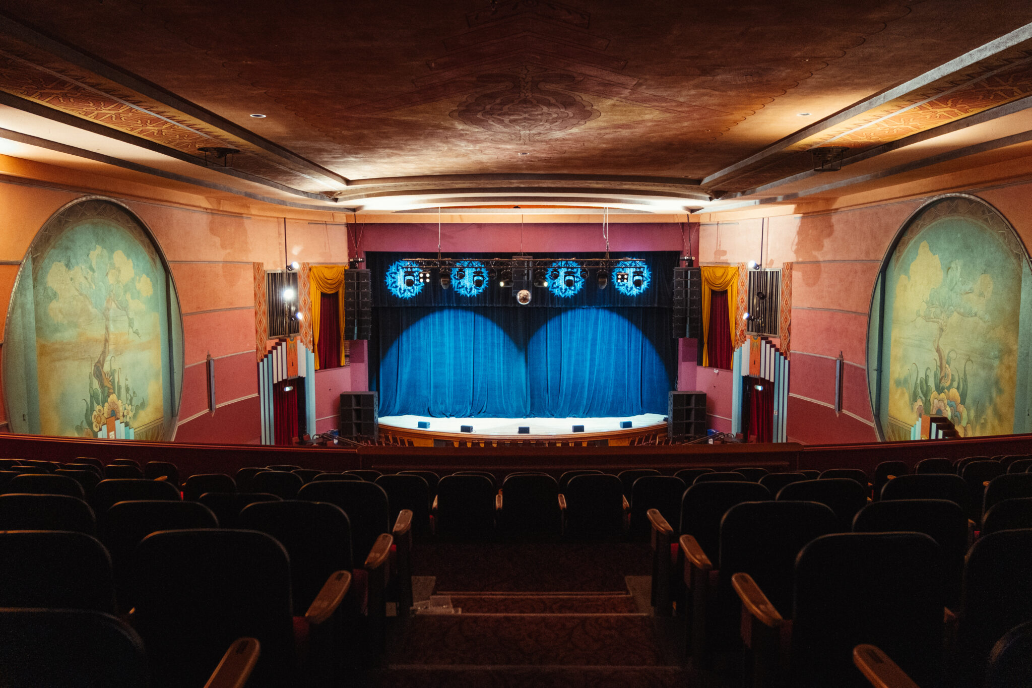 Empty theater from the back facing the stage, blue curtain and murals