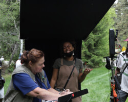 Script supervisor Donna Parish (center, left) and fellow Zandashé Brown (center, right) work together on the set of 'The Matriarch.' Photographer: Ash Gerlach Crew members standing outdoors near a viewing monitor and script station