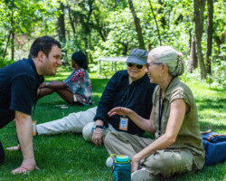 Lab fellow Hasan Hadi (left) converses with creative advisors Hilary Brougher (middle) and Pamela Martin (left). Photographer: Jonathan Hickerson Hasan Hadi talks with advisors as they sit cross-legged in the grass