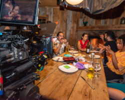 On the set of Michael León's 'Crabs in a Barrel' during the 2022 Directors Lab. Photographer: Jonathan Hickerson A camera on the left looking over actors seated at a long dinner table