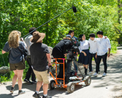 On the set of Neo Sora's 'Earthquake' during the 2022 Directors Lab. Photographer: Sam Emenogu Camera and crew move alongside the camera dolly in a green outdoor space