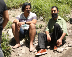 Lab fellow Edwin Martinez (left) and editor and producer Fahd Ahmed (right) after the Stewart Falls hike during the 2022 Documentary Edit and Story Lab. Photographer: Maya Dehlin Edwin sits barefoot on a rocky hill near Fahd