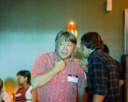 A candid capture of Ham Tran during a festival lunch event. Photographer: Herka Yanis Pangaribowo Ham stands wearing a red patterned shirt amid blue-tinted light